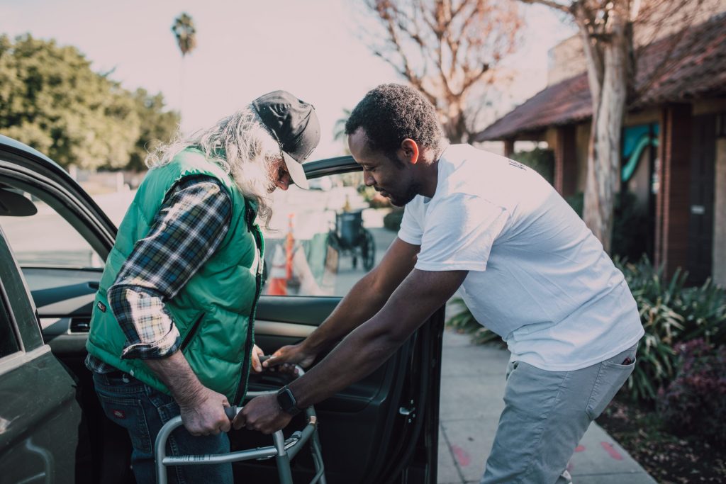 man helping another man with a walker exit a vehicle